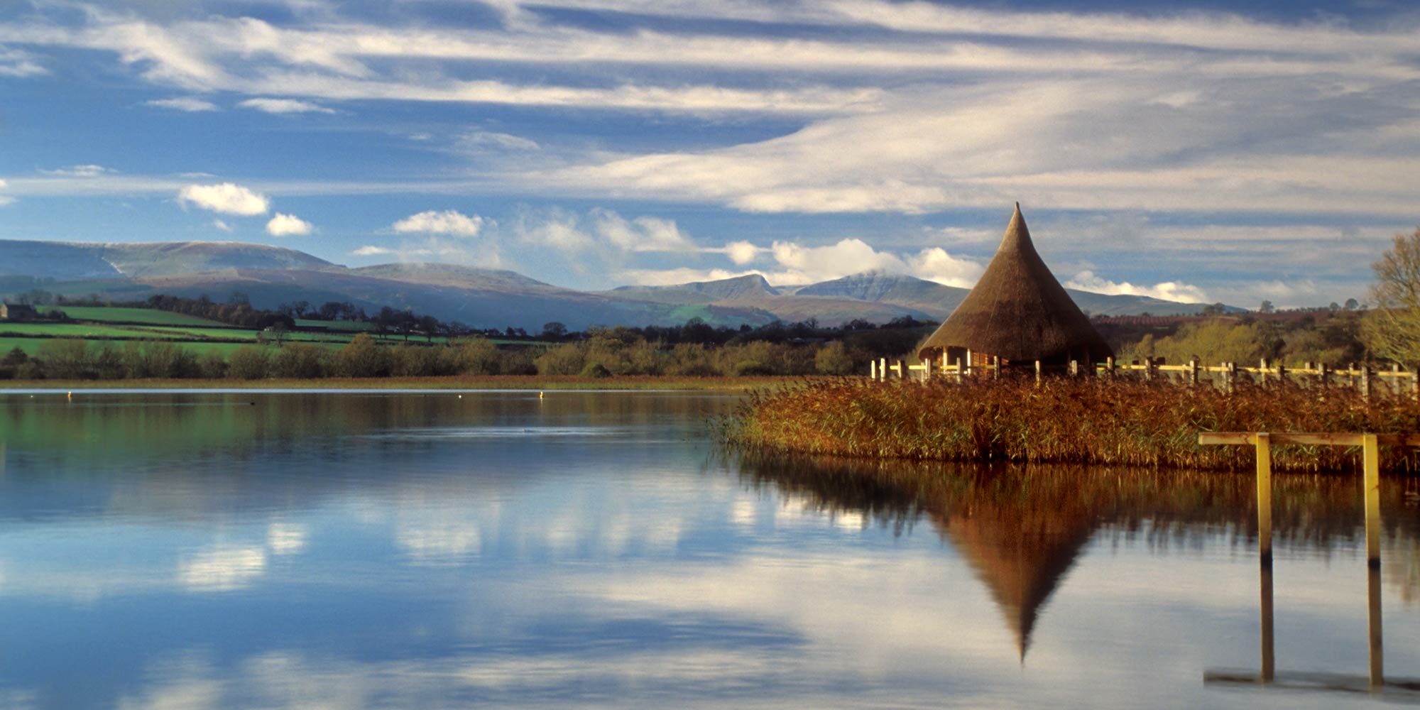 A thatched roundhouse reflected in a lake