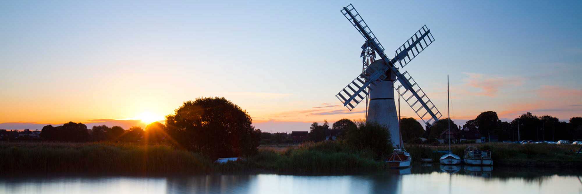 Windmill reflected in still lake with the sun setting on the horizon