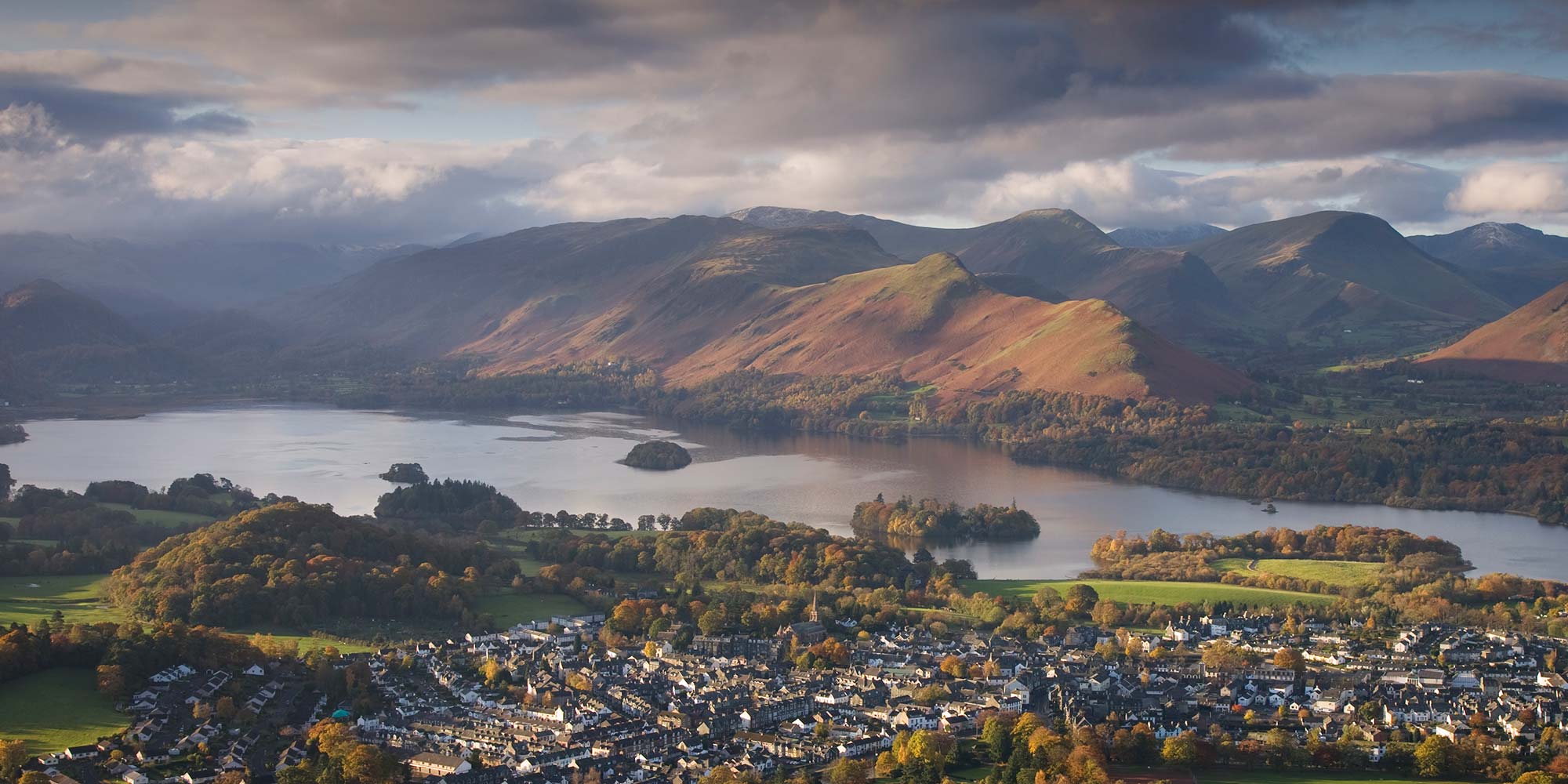 View over a lake nestled between high fells with a town on the near shore