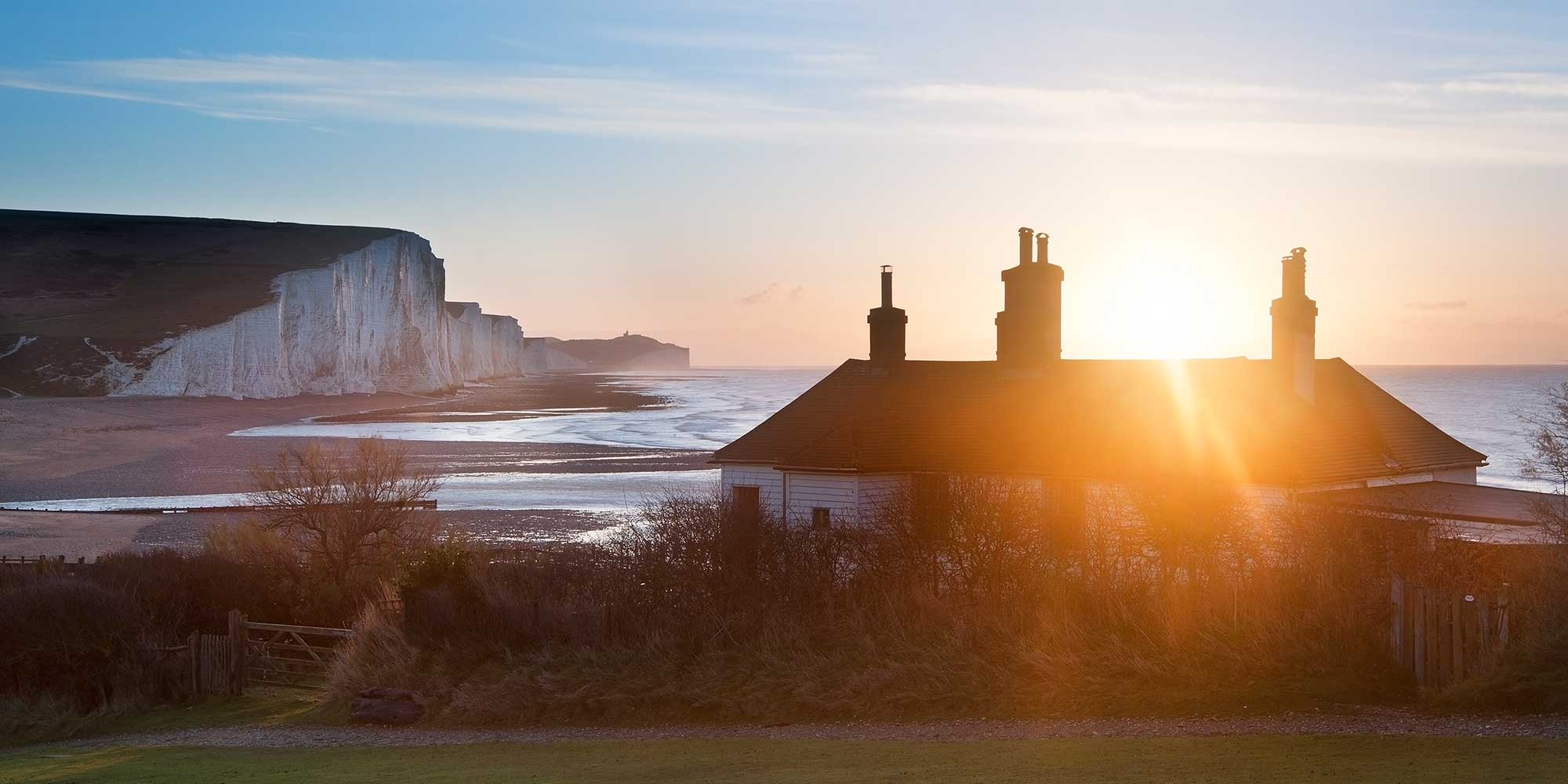 Sheer chalk cliffs with the sun setting over a nearby house