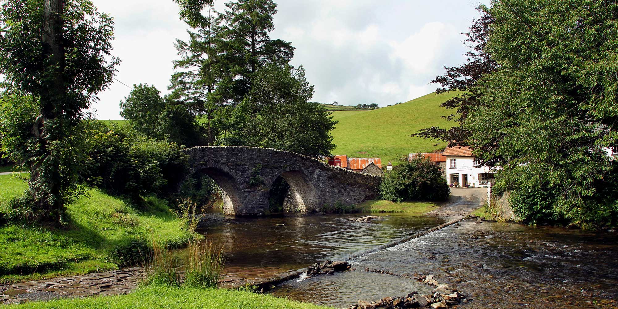 Stone bridge over a river, with a cottage on the far riverbank